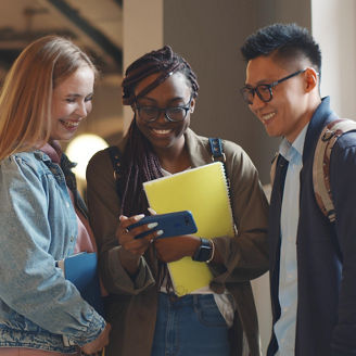 Happy young university students friends relaxing with smartphone in corridor. Multiethnic hipster college people watching video on smartphone and laughing resting after lecture in hallway
