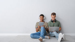 Teenage boys with different devices sitting near light wall
