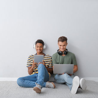 Teenage boys with different devices sitting near light wall
