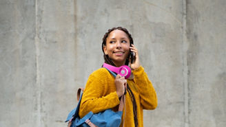 Full body side portrait of young african woman carrying a bag talking on mobile phone outdoors in city