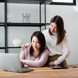 Asian mother and teenage daughter looking at laptop computer at home office, happy family work together, middle age woman and teen they shoping online on computer