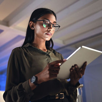 Tablet, designer and serious woman research in business startup office at night on deadline. Technology, creative professional or Indian entrepreneur reading information, email or app in neon company.