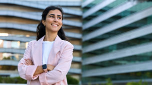 Confident portrait of young middle eastern Israel businesswoman standing with crossed hands at office building. Successful smiling indian or arabic woman in business suit looking aside. Copy space