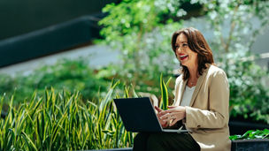 Woman working on laptop surrounded by greenery