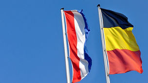 A flag of Belgium and one of the Netherlands under a blue sky