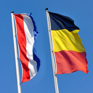 A flag of Belgium and one of the Netherlands under a blue sky