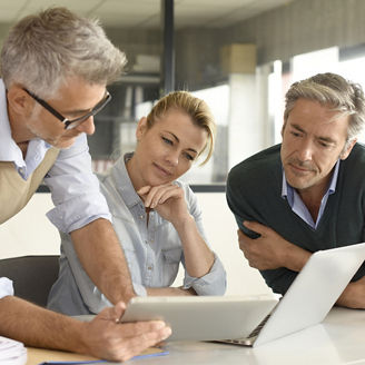 Three businesspeople look at a tablet and laptop together.