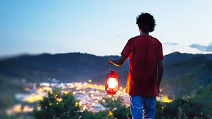 Man holding lantern on a hill over-looking over lit up city