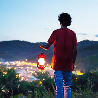 Man holding lantern on a hill over-looking over lit up city