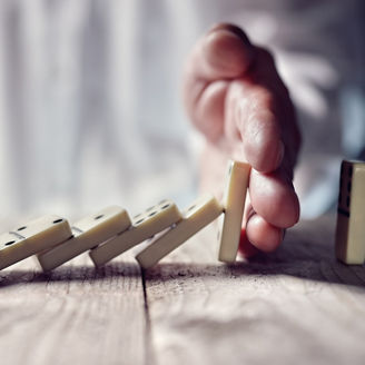 Man’s hand stopping chain of dominos from falling