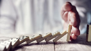 Man’s hand stopping chain of dominos from falling