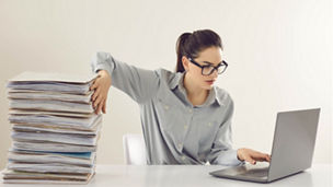 Woman holding a stack of documents while working on laptop