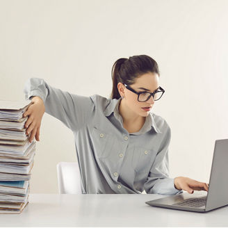 Woman holding a stack of documents while working on laptop