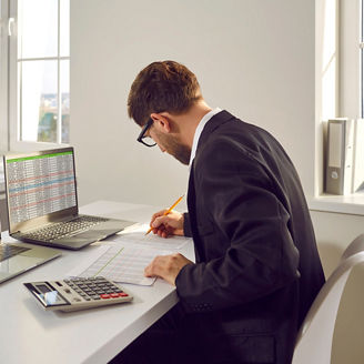 A man is working on his laptop with a calculator next to him