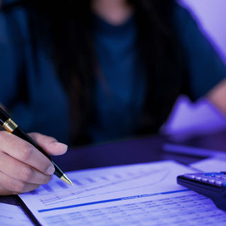 A woman is typing something on a calculator and writing something down on paper.