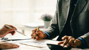 Close-up of people working at a desk with papers and a calculator 