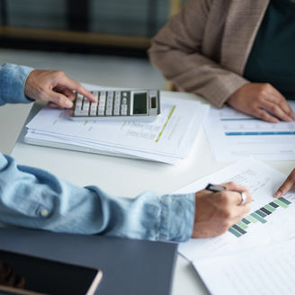 Two people pointing at graphs on papers and calculating something on a calculator