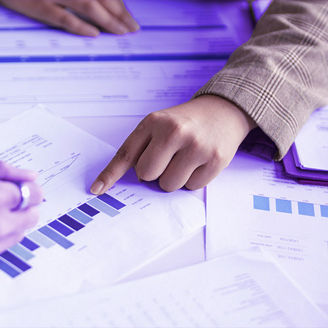 Two people pointing at graphs on papers and calculating something on a calculator
