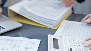 People are sitting at a table with papers and calculators on the table.