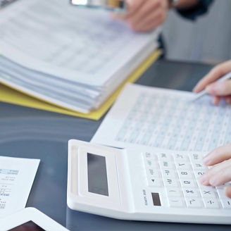 People are sitting at a table with papers and calculators on the table.