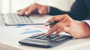 A mans hand is typing something on a calculator