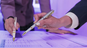 Two hands hold pens, pointing at something on paper