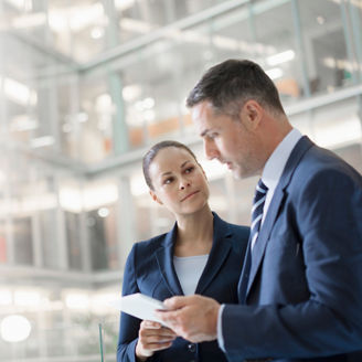 Businessman and businesswoman looking at digital tablet in lobby --- Image by © Hiya Images/Corbis