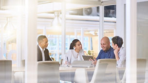 Corporate business meeting in modern office with glass walls, flare from the sunlight and reflections on the glass while business discussions take place amongst board members.