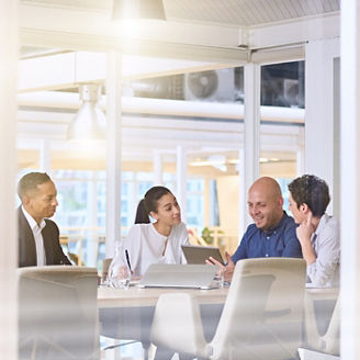 Corporate business meeting in modern office with glass walls, flare from the sunlight and reflections on the glass while business discussions take place amongst board members.