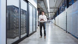 man standing in a server room, looking at a display 