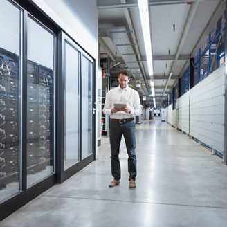 man standing in a server room, looking at a display 