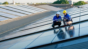 Two solar panel technician are holding laptop next to solar panels