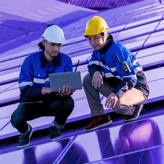 Two solar panel technician are holding laptop next to solar panels