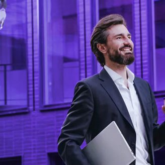 Man walking in front the building while holding a cup of coffee and laptop