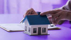 Handen die een paper vasthouden op tafel en een klein huis dat op tafel staat