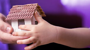 De handen van een vrouw en kind houden een miniatuurhuisje vast