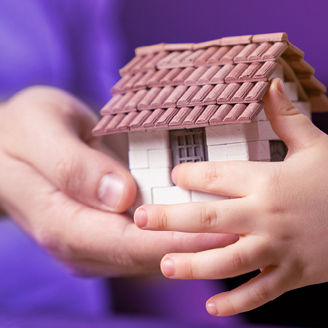 De handen van een vrouw en kind houden een miniatuurhuisje vast