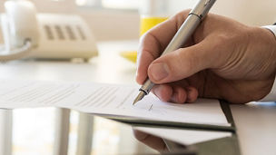 Een man zit aan een bureau en ondertekent een papier.