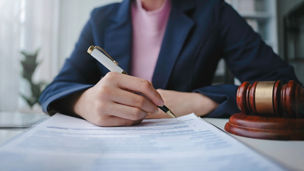 A woman is writing something down on paper next to a judge’s gavel.