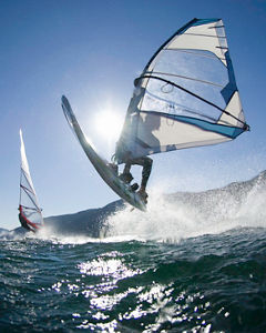 Man jumping wave on windsurf board, rear view