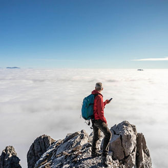 Hiker on top of the mountain with blue clear sky over clouds using smart phone