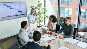 Senior female ceo and multicultural business people discussing company presentation at boardroom table. Diverse corporate team working together in modern meeting room office. Top view through glass