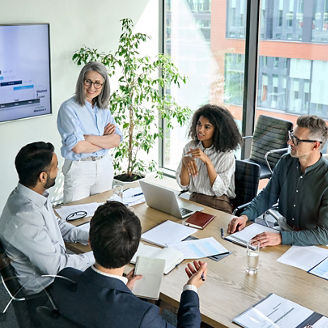Senior female ceo and multicultural business people discussing company presentation at boardroom table. Diverse corporate team working together in modern meeting room office. Top view through glass