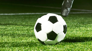 Close up of a soccer player who is about to kick a ball. It is placed on the grass in a soccer stadium at night.