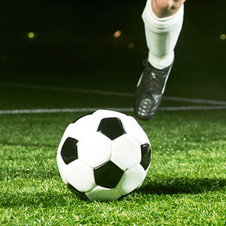 Close up of a soccer player who is about to kick a ball. It is placed on the grass in a soccer stadium at night.