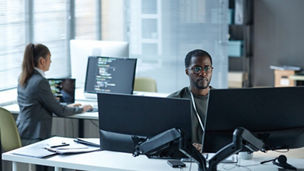 Portrait of Black young man as IT programmer using multiple computers at workplace in office and reviewing data copy space