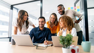 Happy group of Latin American coworkers sharing ideas in a business meeting and smiling while using a laptop