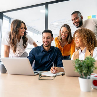 Happy group of Latin American coworkers sharing ideas in a business meeting and smiling while using a laptop