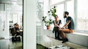 Two young start up business people sitting in a huge office window and talking