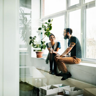 Two young start up business people sitting in a huge office window and talking